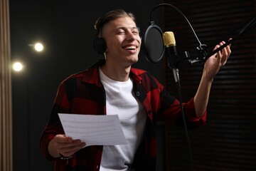 Singer with sheet recording song in professional studio