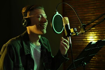 Vocalist with headphones singing into microphone in professional record studio
