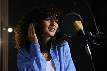 Vocalist with headphones singing into microphone in professional record studio