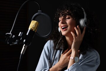 Vocalist with headphones singing into microphone in professional record studio