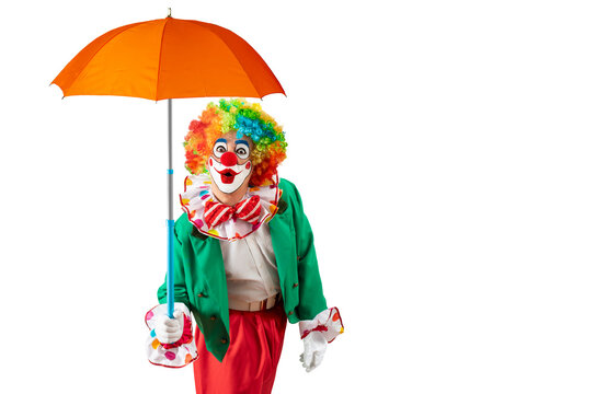 Clown holding orange umbrella. Entertainer Joker in colorful suit and wig. Buffoon with clown whiteface makeup. Professional actor at event, kid's party, circus