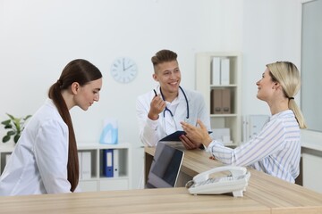 Obraz premium Professional receptionist and doctor working with patient at wooden desk in hospital