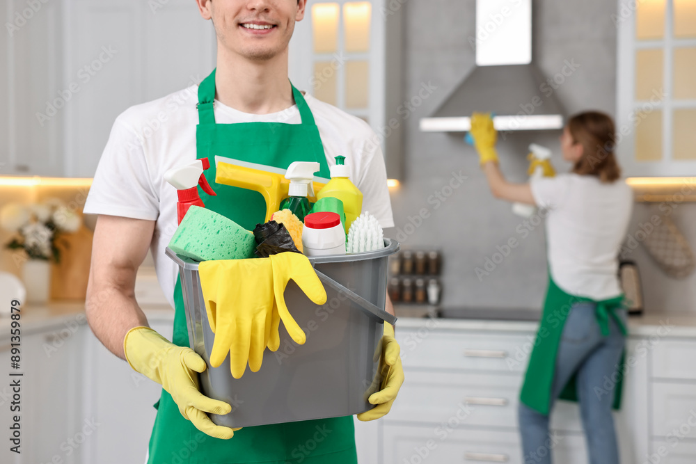 Wall mural Cleaning service worker holding bucket with supplies in kitchen, closeup