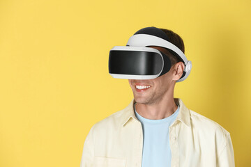 Smiling man using virtual reality headset on yellow background, space for text