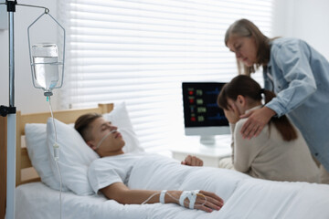 Fototapeta premium Coma patient. Sad women near unconscious young man in hospital