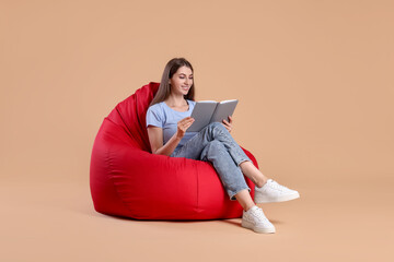 Smiling woman reading book on red bean bag chair against beige background