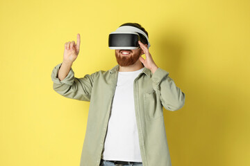 Happy man using virtual reality headset on pale yellow background