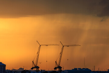 Two cranes are silhouetted against a cloudy sky