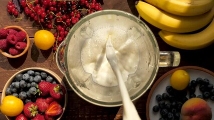 Pouring fresh cow's milk into a blender while preparing a cocktail with the addition of fruits and berries. Organic smoothie for a healthy lifestyle. diet and healthy food. Top view - Powered by Adobe