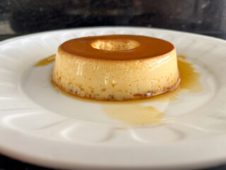 A smooth, golden flan with a caramelized top on a white plate.