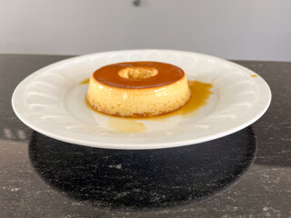 A single serving of creamy flan on a white plate.