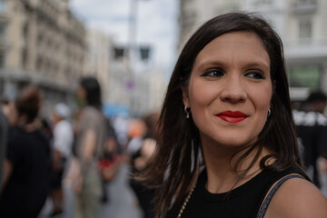 Young woman smiling with red lipstick in a blurred crowd. Young woman is smiling slightly while standing in a busy crowd in an urban environment