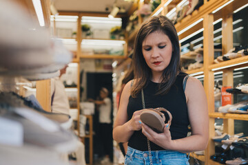 Woman deciding on which sandals to buy in shoe store. Woman holding a sandal in her hand while shopping in a shoe store