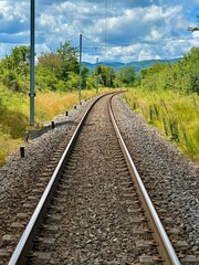 Curved Railway Track Surrounded by Lush Greenery and Scenic Landscape Under a Vibrant Blue Sky with Fluffy Clouds