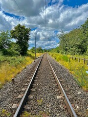 Fototapeta premium Curved Railway Track Surrounded by Lush Greenery and Scenic Landscape Under a Vibrant Blue Sky with Fluffy Clouds