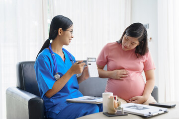 Obraz premium Pregnant mothers meet the nurse at the clinic as scheduled, reviewing their medical history and discussing symptoms. Sitting on the sofa, they report headaches, nausea, and back pain to the nurse.