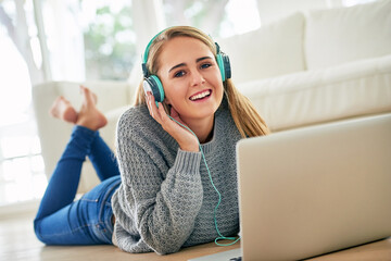 Portrait, woman and relax with headphones on laptop for listening music, streaming online and podcast audio in lounge. Smile, female person and earphones with digital for browsing internet at house