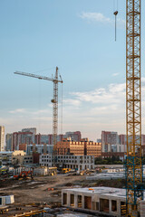 Construction site in the middle of the city in the summer evening. Tower cranes, hydraulic shovel,...