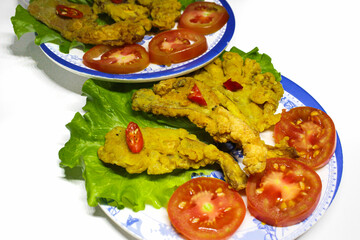 Photo of crispy fried mushroom food served on a plate and a bowl of sauce decorated with tomatoes and chilies on the side, on a white background. isolated