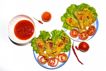 Photo of crispy fried mushroom food served on a plate and a bowl of sauce decorated with tomatoes and chilies on the side, on a white background. isolated