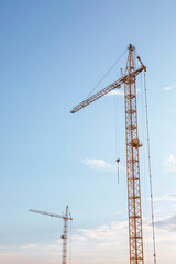 Two tower cranes on the evening blue sky background, vertical photo.