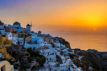 Fototapeta premium Sunset in Oia village on Santorini, Greece. Famous Santorini sunset capture. Windmills and churches in the background. Blue dome church.