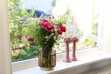 Beautiful ranunculus flowers and chamomiles in vase on windowsill indoors