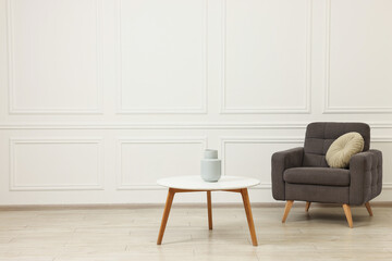 Soft armchair, coffee table and vase in stylish room. Space for text