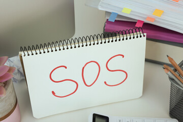 Notebook with word SOS and stationery on white table at workplace