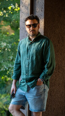 A charismatic middle-aged man, slightly overweight, posing in front of a scenic window with the evening sun shining through