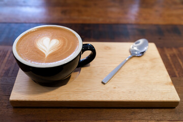 Latte coffee or cappuccino coffee in black cup with beautiful heart latte art on wooden table.
