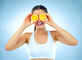 Woman, orange and face in studio for health, diet and detox for wellness on blue background. Fruit,...