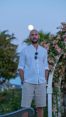 A charismatic middle-aged man posing stylishly in a scenic park, with the full moon in the sky