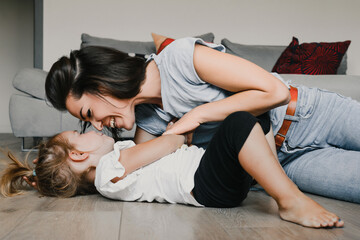 Young mother is lying on the floor playing with her toddler daug