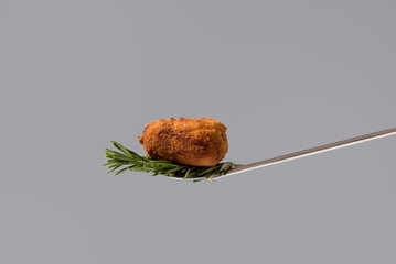 Croqueta frita sobre una cuchara aperitivo en fondo gris