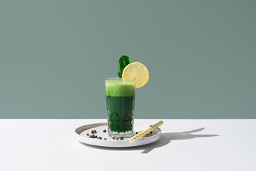 Jugo batido de espinacas adornado con una rodaja de limón sobre una mesa blanca y fondo verde	