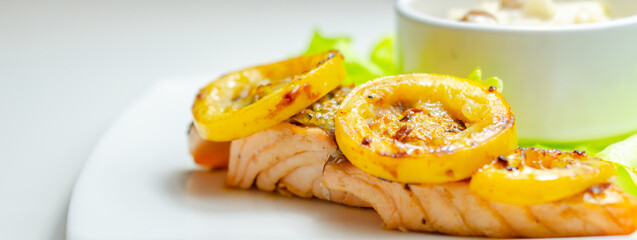 A plate of food with a piece of salmon and a couple of yellow slices of lemon