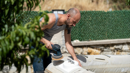 The moment when a man is sanding his boat with an electric sander in the garden of his house