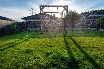Obraz premium Grass swing sprinkler watering the lawn in the backyard of a house.