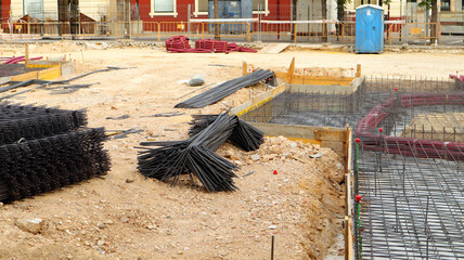 Pile of rebar sits on the ground next to wooden formwork in construction site. Other construction...