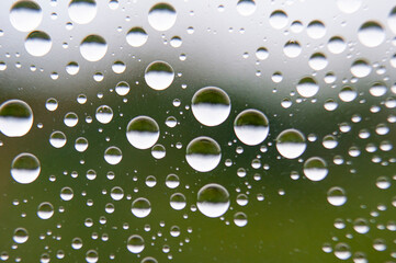 Straight view of water droplets on clear glass on blurred nature background. Suitable for design and wallpaper.