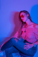 High Fashion model woman in colorful bright neon blue and purple lights posing in studio. Portrait of beautiful woman with trendy glowing make-up.