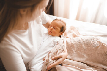 Mother holding infant baby boy sleeping and frowning on hands in room. Motherhood.