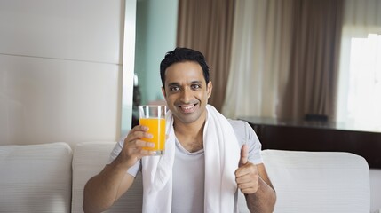 Fototapeta premium An Indian man smiling and holding up an orange juice glass at home, showing happiness, enjoying a drink, relaxed atmosphere