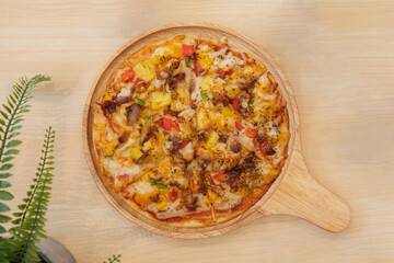 Hawaiian pizza with grilled pork on a wooden plate ready to serve.
