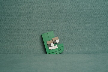 Miniature figure of the letter L against a greenish fabric background