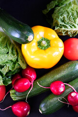 vegetables on a black background. Zucchini, peppers, radishes, cabbage.
