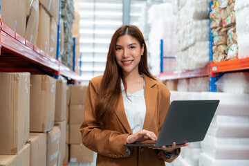 Smiling businesswoman using a laptop in a warehouse, showcasing modern inventory management and...