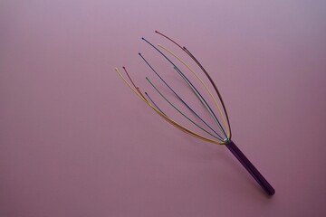Scalp massager with Masseur for a head against pink background. Wire head massage device. Brush for hair growth stimulating brush. Hair massage. stimulating brush. Hair care, head relaxation