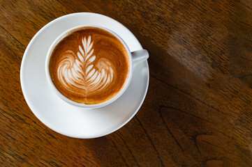 Latte art coffee in a ceramic mug On the wooden table in the soft sunlight